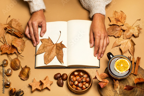 Manos de mujer con un libro abierto, hojas secas, taza de café sobre un fondo marrón. Vista superior. Concepto: Estilo de vida Otoño Invierno