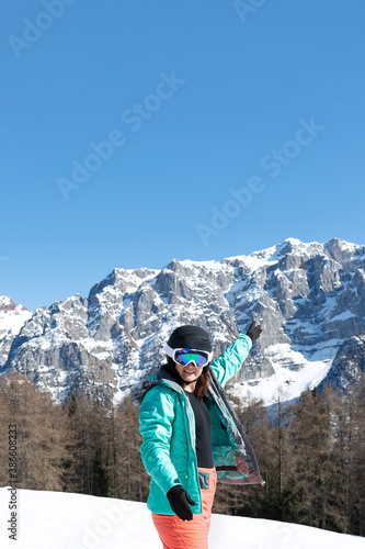 A woman in a colorful ski suit, helmet and sunglasses after skiing stands against the backdrop of mountain peaks. Sports concept, people, travel.