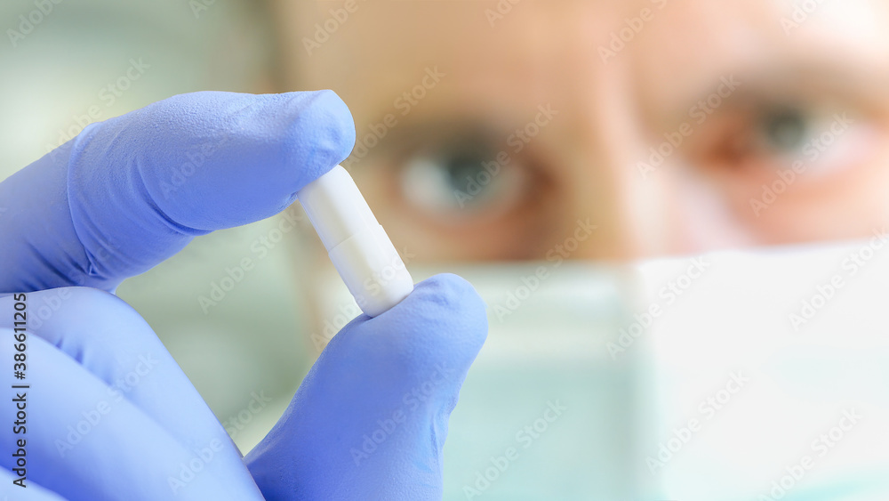 Scientist with medical mask showing white pill. Research concept. Selective focus. Scientist with medical mask showing white pill. Research concept. Selective focus.