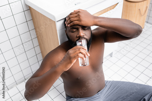 afro-american man suffering from hangover and drinking water