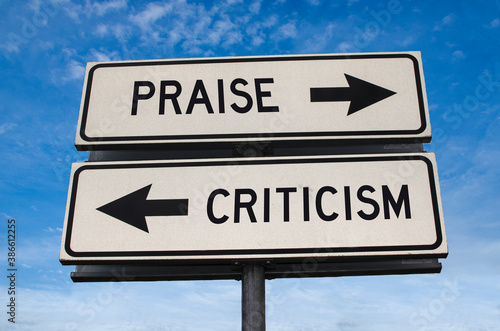 Praise vs criticism. White two street signs with arrow on metal pole with word. Directional road. Crossroads Road Sign, Two Arrow. Blue sky background. Two way road sign with text.