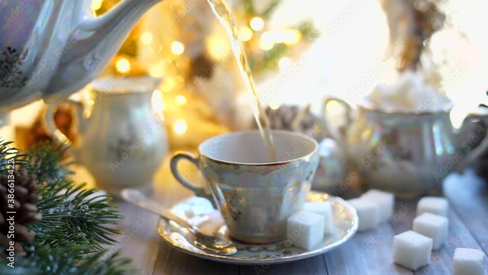 Traditional English tea is poured into a cup from a Chinese porcelain set in a Christmas decor. Traditional English tea is poured into a cup from a Chinese porcelain set in a Christmas decor.