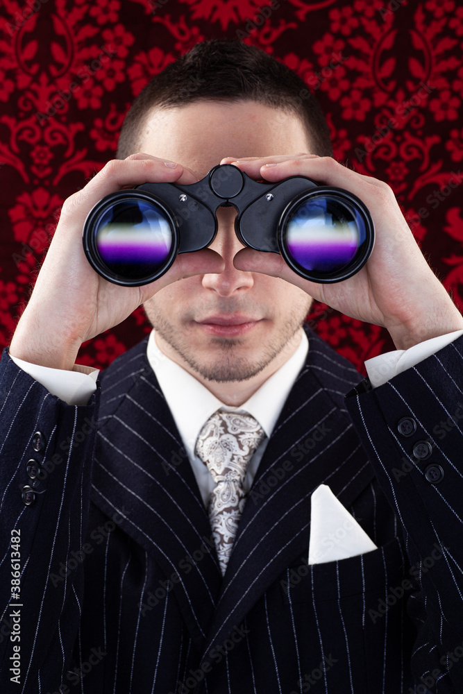 Studio photo of a dark man with business suit looking through binoculars.