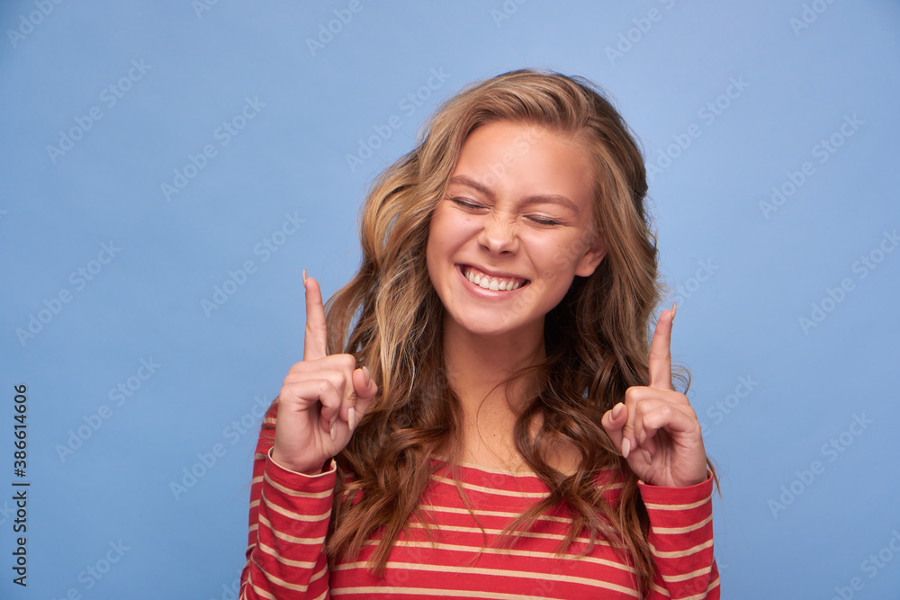 Close up photo of an attractive excited girl with straight index fingers eyes closed and tongue showing empty space show novelty banner dressed in red clothes with yellow stripes on a blue background Close up photo of an attractive excited girl with straight index fingers eyes closed and tongue showing empty space show novelty banner dressed in red clothes with yellow stripes on a blue background
