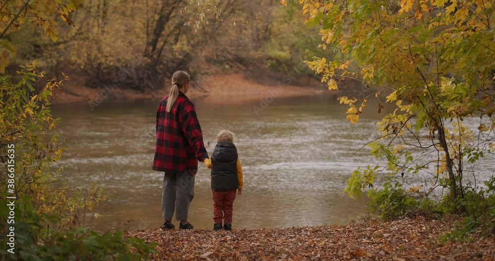 woman with her little child at nature, people are standing on coast of picturesque forest pond at autumn day woman with her little child at nature, people are standing on coast of picturesque forest pond at autumn day