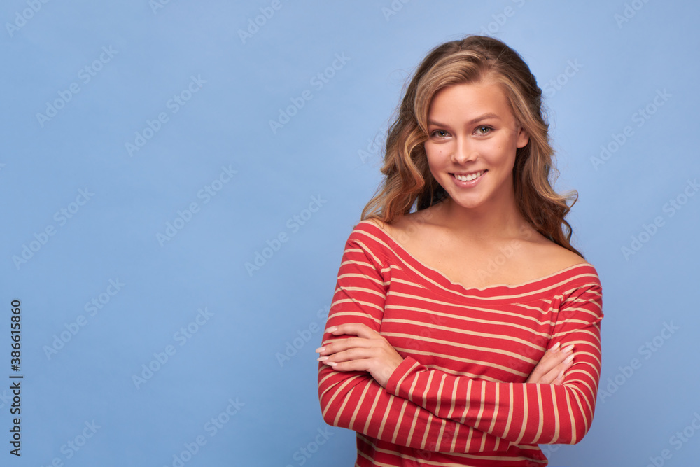 Portrait of a smiling girl with her hands on her waist in red clothes with yellow stripes looking at the camera lens on a blue background Portrait of a smiling girl with her hands on her waist in red clothes with yellow stripes looking at the camera lens on a blue background