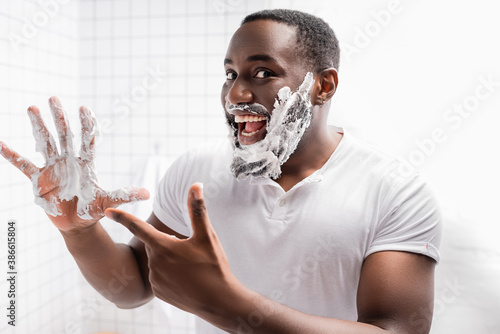 happy afro-american man with shaving foam on face pointing at hand