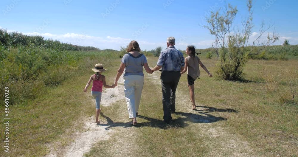 Active happy and healthy elderly European couple on a walk with their two granddaughters enjoying beautiful landscape. Tracking shot, rear view. slow motion 4k 50 fps Active happy and healthy elderly European couple on a walk with their two granddaughters enjoying beautiful landscape. Tracking shot, rear view. slow motion 4k 50 fps