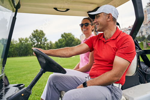 Konstfotografi Smiling man giving a ride to a lady golfer