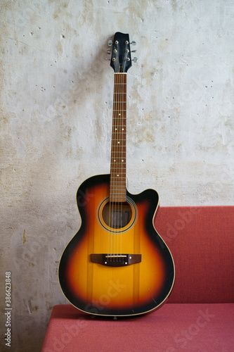 Acoustic vintage black and orange guitar on red couch at loft style apartment over concrete wall . Vertical. © DimaBerlin
