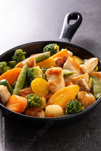 Stir fry chicken with vegetables on iron pan on black stone 