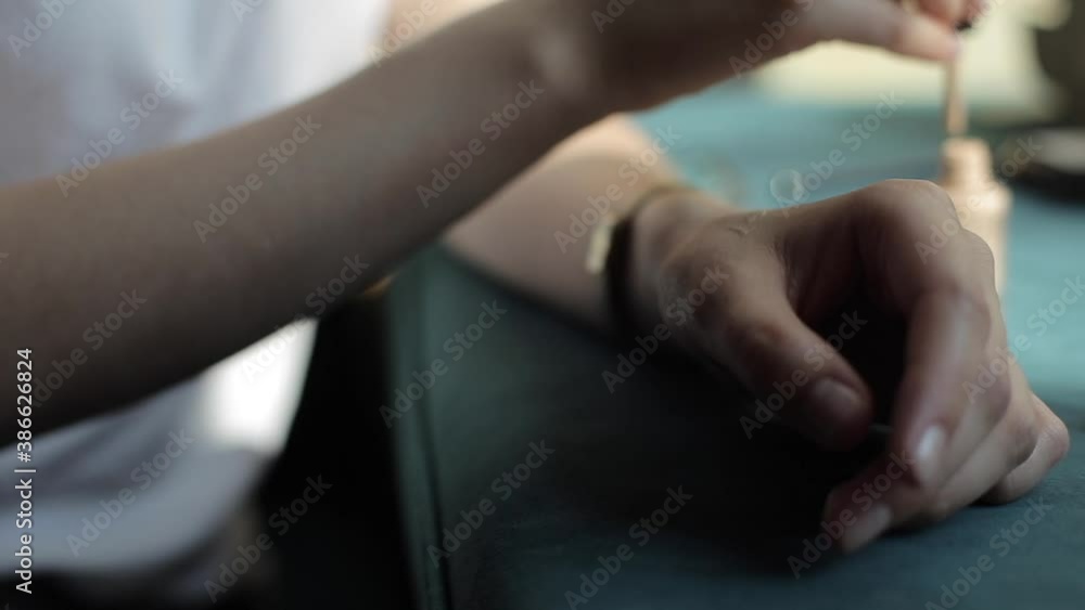 A young woman in a white T-shirt sits at a table and applies foundation from a jar to her hand. Close-up of hands. Blurred background A young woman in a white T-shirt sits at a table and applies foundation from a jar to her hand. Close-up of hands. Blurred background