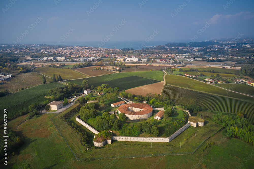 Fototapeta premium Forte Ardietti rises between the territories of Peschiera del Garda and Ponti sul Mincio, Italy. Aerial view of the fortress surrounded by vineyards. Fortified Austrian fort top view on the hill.