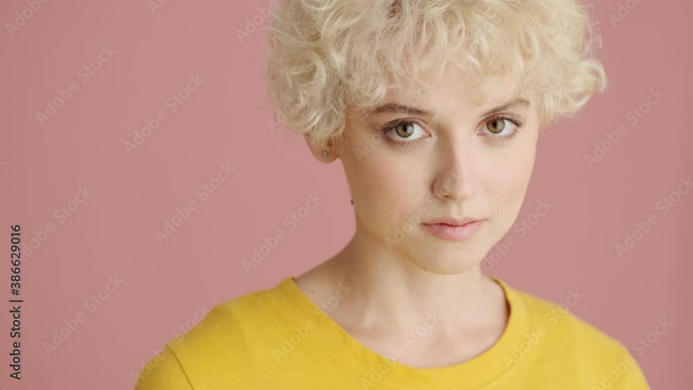 A close-up view of a smiling young woman is opening her eyes and looking to the camera standing isolated over pink background A close-up view of a smiling young woman is opening her eyes and looking to the camera standing isolated over pink background