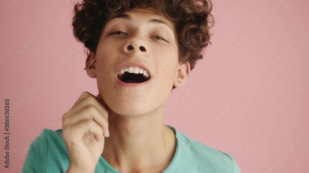 A close-up view of a happy curly boy is looking at his hairstyle standing isolated over pink background A close-up view of a happy curly boy is looking at his hairstyle standing isolated over pink background