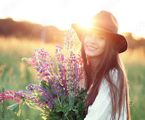 Girl with lupines in shirt and hat at sunset