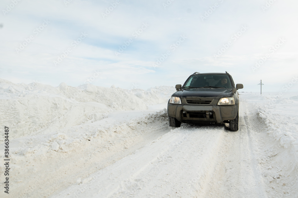 Male driver in a black dirty car on a winter road cleared of snow, drifts along the road
