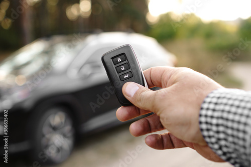 Man hand holds car key against blurred car. New car concept.