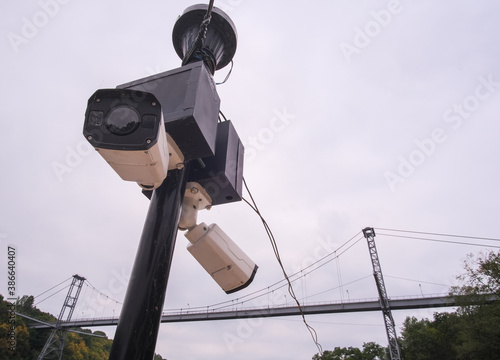 Security camera hanging among wire in guarded bridge with cloudy sky background.
