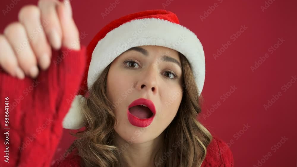 A positive woman wearing a warm red sweater and christmas hat is knocking on the door standing isolated over red background A positive woman wearing a warm red sweater and christmas hat is knocking on the door standing isolated over red background