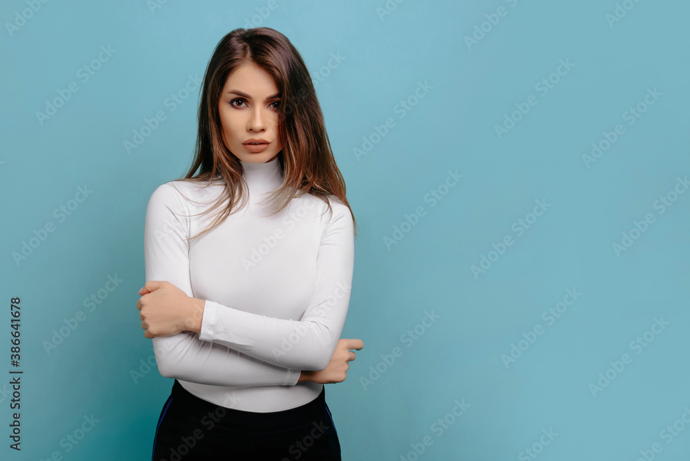 Portrait of serious sensual beautiful caucasian woman in white turtleneck looking at camera with folded hands, isolated on pastel blue background. People lifestyle concept. Mock up copy space. Holding Portrait of serious sensual beautiful caucasian woman in white turtleneck looking at camera with folded hands, isolated on pastel blue background. People lifestyle concept. Mock up copy space. Holding