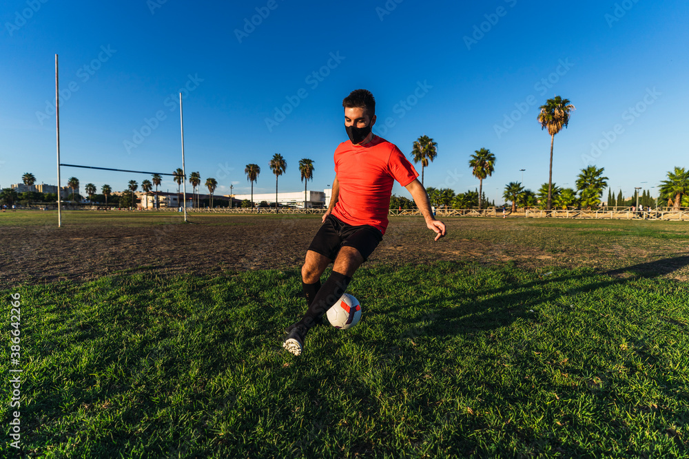 Chico joven con mascarilla por el covid 19 preparandose y jugando al futbol Chico joven con mascarilla por el covid 19 preparandose y jugando al futbol