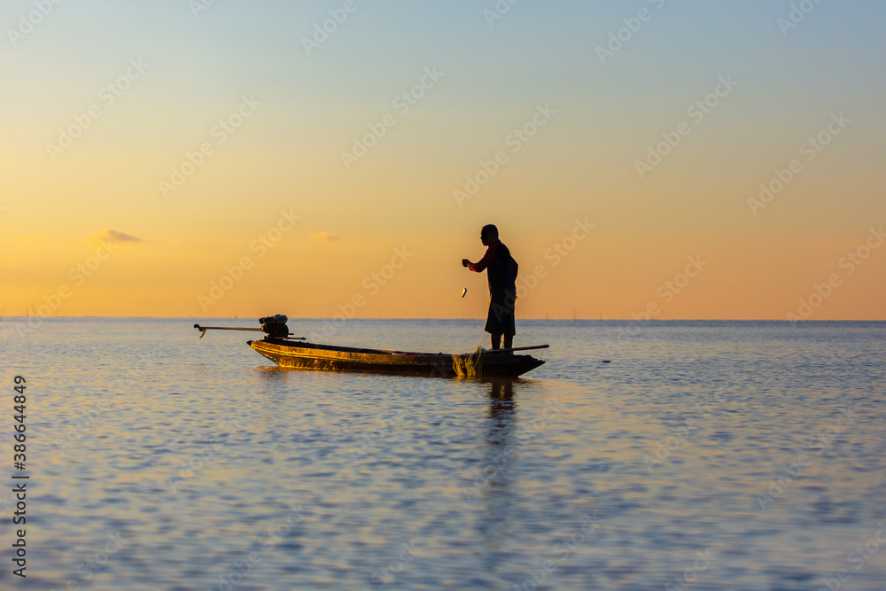 Silhouette of asian Fisherman on a traditional wooden boat during sunrise.
