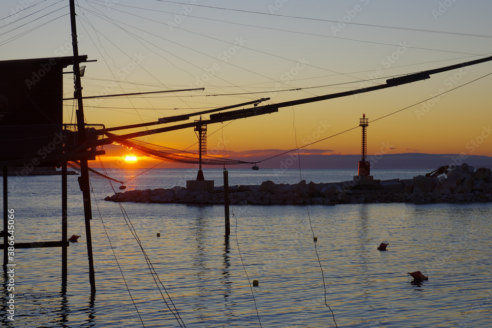 Termoli - Molise - Silhouette of an ancient fishing machine (trabucco), in the background the sun rising over the sea.