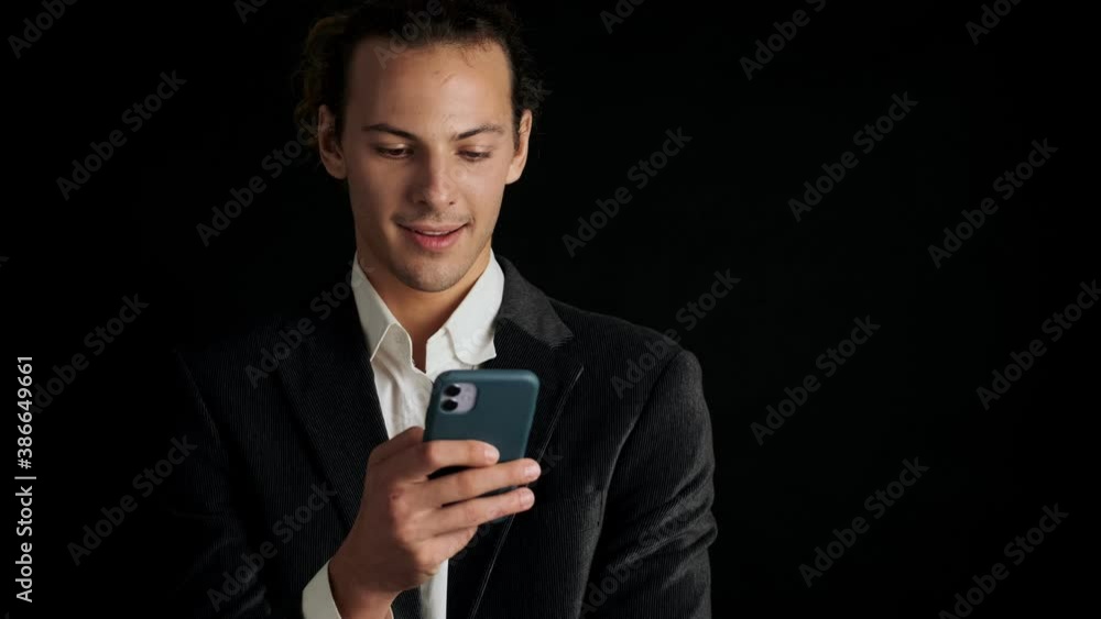 Young handsome concentrated man in a suit using mobile phone isolated over black background Young handsome concentrated man in a suit using mobile phone isolated over black background