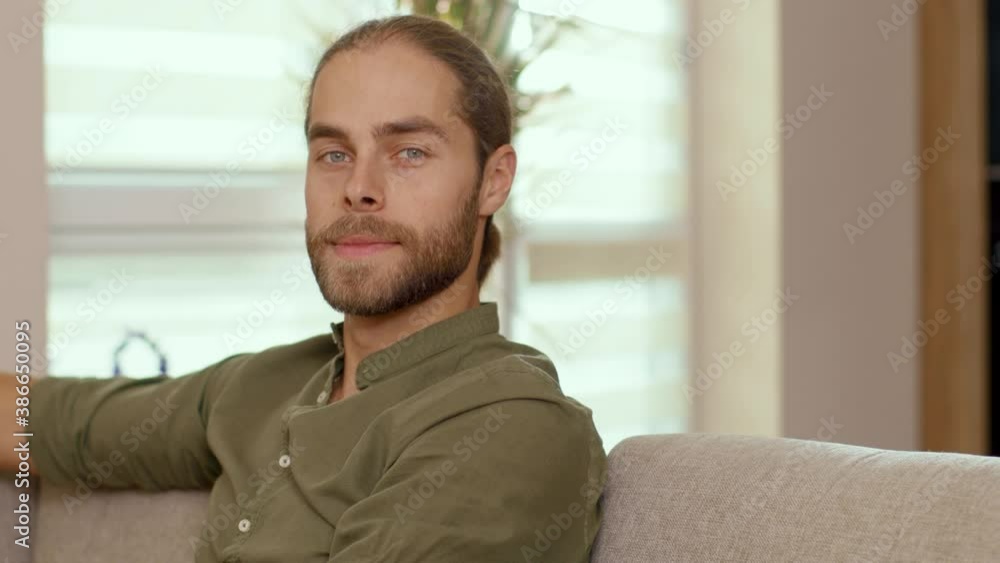 Portrait of attractive happy caucasian guy with ponytail smiling to camera enjoying cozy atmosphere at home. Casual people lifestyle. Handsome face. Youth concept. Portrait of attractive happy caucasian guy with ponytail smiling to camera enjoying cozy atmosphere at home. Casual people lifestyle. Handsome face. Youth concept.