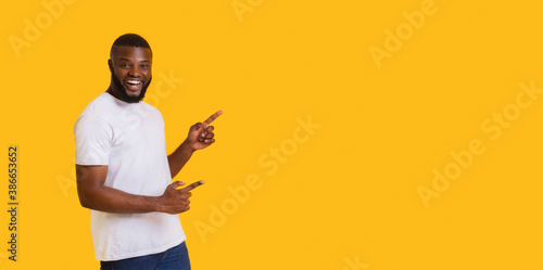 Happy black guy pointing at copy space on yellow