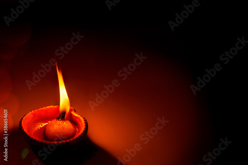 Happy Diwali - One Diya oil clay lamp illuminated as a religious tradition during Diwali celebration with copy space. Hindu culture ritual festive celebration during corona pandemic at home.