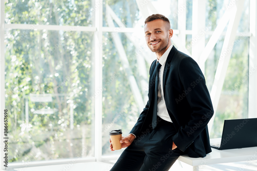 Happy handsome businessman relax with cup of coffee in hand during break time in modern office with copy space Happy handsome businessman relax with cup of coffee in hand during break time in modern office with copy space