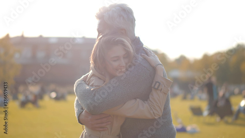Side view of senior man and adult daughter meeting in park and hugging