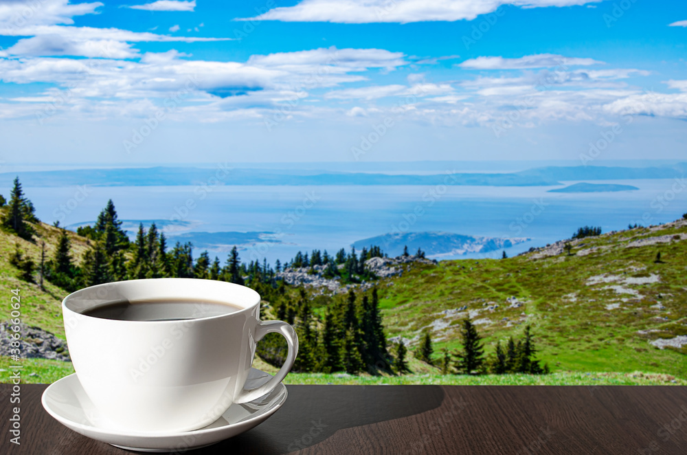 Cup of coffee on the table against mountains background. View of blue sea and green valley in the mountains. Cup of coffee on the table against mountains background. View of blue sea and green valley in the mountains.