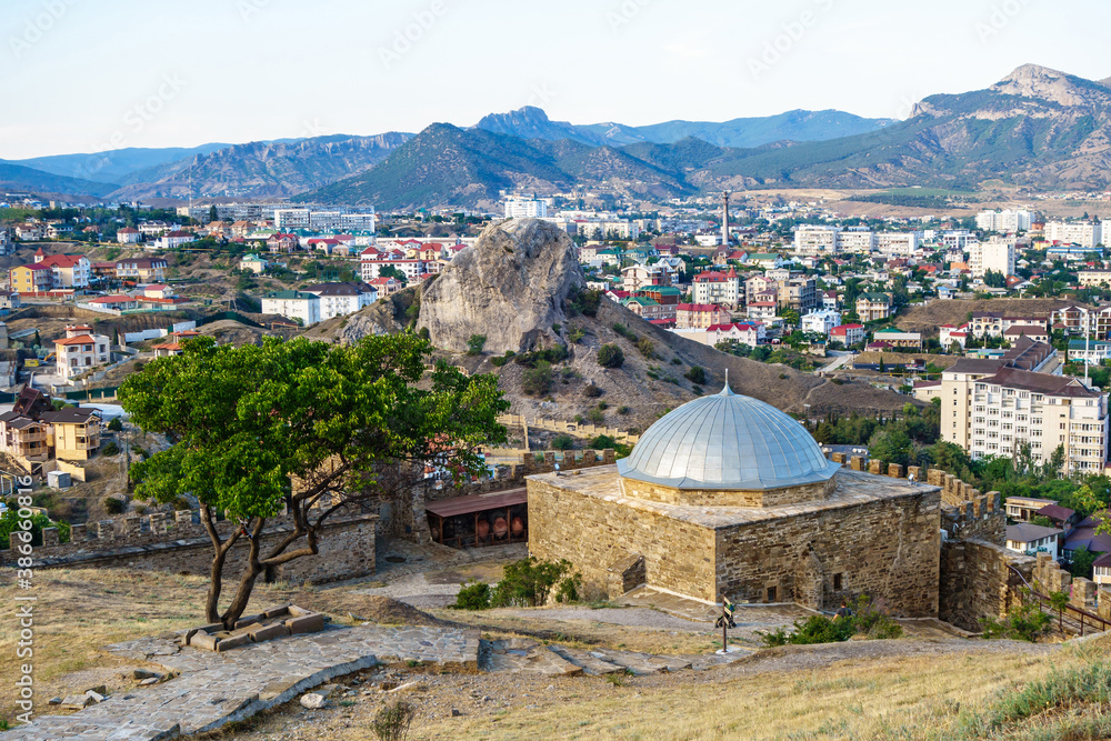 Naklejka premium Panorama of resort town Sudak, Crimea. Padishah Jami mosque & walls of Genoese fortress on foreground. Streets of city & rock Sugar Head are on background