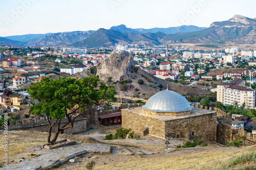 Panorama of resort town Sudak, Crimea. Padishah Jami mosque & walls of Genoese fortress on foreground. Streets of city & rock Sugar Head are on background
