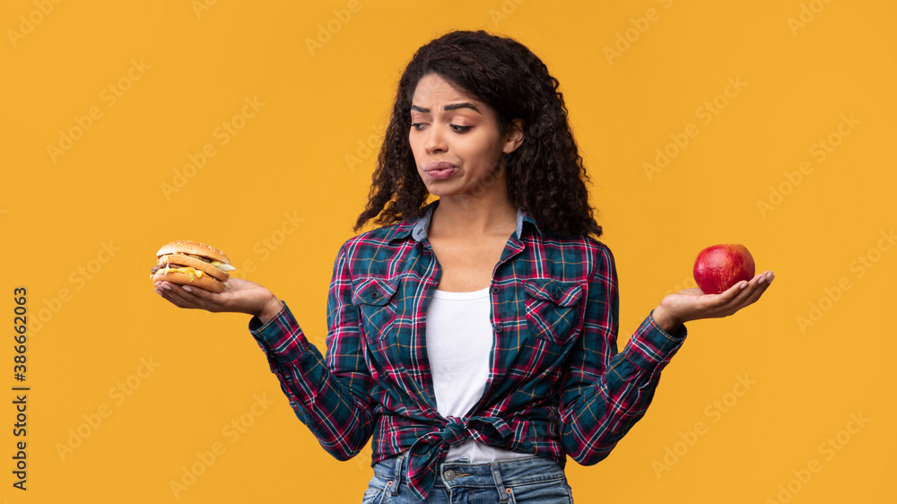 Hungry Black Woman Holding Burger And Apple Fruit - obrazy, fototapety, plakaty 