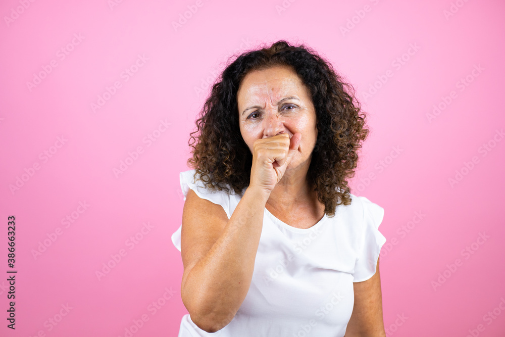 Middle age woman wearing casual white shirt standing over isolated pink background with her hand to her mouth because she's coughing Middle age woman wearing casual white shirt standing over isolated pink background with her hand to her mouth because she's coughing