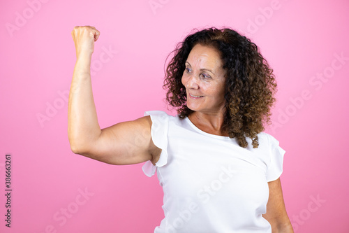 Middle age woman wearing casual white shirt standing over isolated pink background showing arms muscles smiling proud