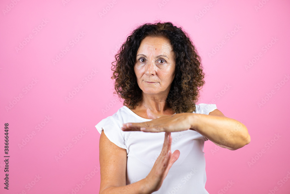 Middle age woman wearing casual white shirt standing over isolated pink background Doing time out gesture with hands, frustrated and serious face Middle age woman wearing casual white shirt standing over isolated pink background Doing time out gesture with hands, frustrated and serious face
