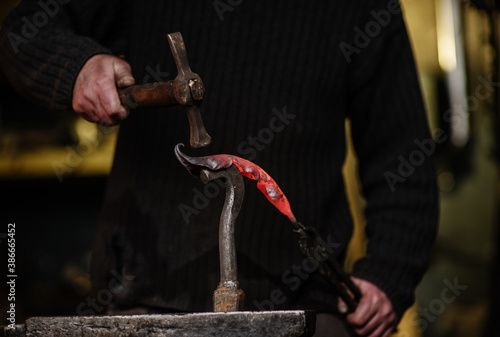 Close-up of the hands of a blacksmith forging a thin iron sheet in the shape of a plant with a hammer on an anvil. Work in the forge photo