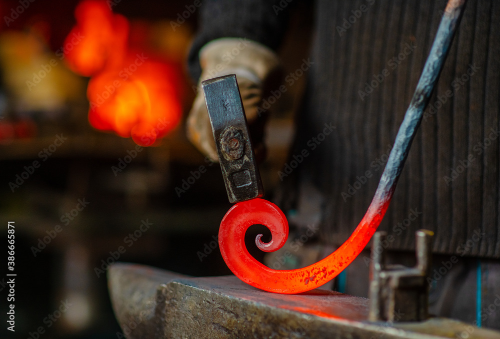 The blacksmith twists the spiral with a sledgehammer, placing a red-hot iron blank on the anvil. Work in the forge