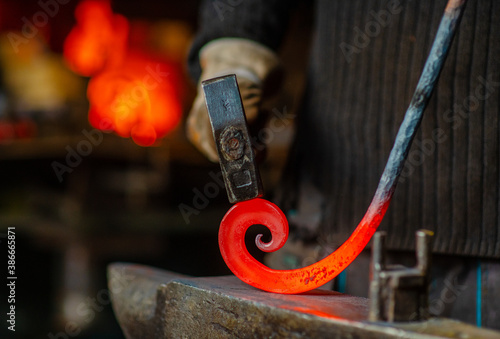 Fotomural The blacksmith twists the spiral with a sledgehammer, placing a red-hot iron blank on the anvil