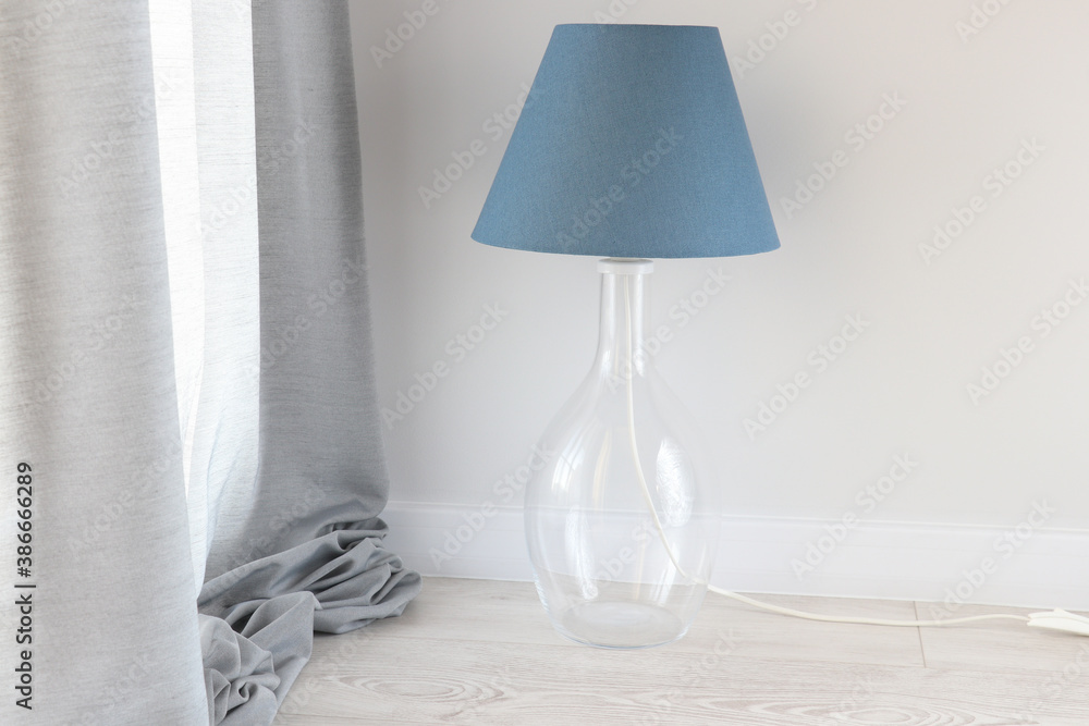 Background with a blue lampshade on the table lamp with a glass element near the light wall and grey cloth. Trendy color in your interior. Background with a blue lampshade on the table lamp with a glass element near the light wall and grey cloth. Trendy color in your interior.
