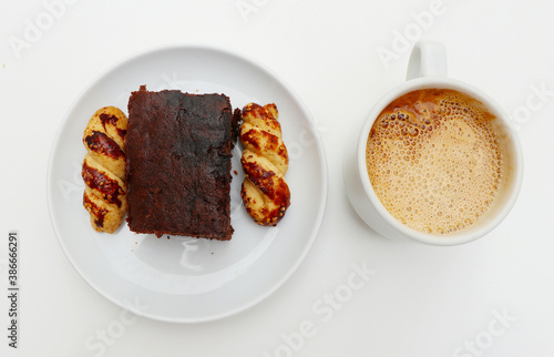 Cup of coffee with cream and plate of cake on a white background