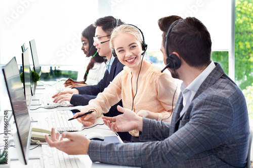 Smiling customer support workers communicating to solve client's problem together at call centre office