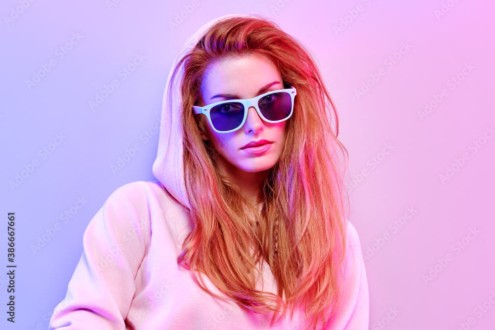 Fashionable hipster woman in Trendy outfit, stylish hair, makeup on pink purple neon light. Redhead model in hoodie, fashion sunglasses. Beautiful girl in autumn fall neon style Fashionable hipster woman in Trendy outfit, stylish hair, makeup on pink purple neon light. Redhead model in hoodie, fashion sunglasses. Beautiful girl in autumn fall neon style