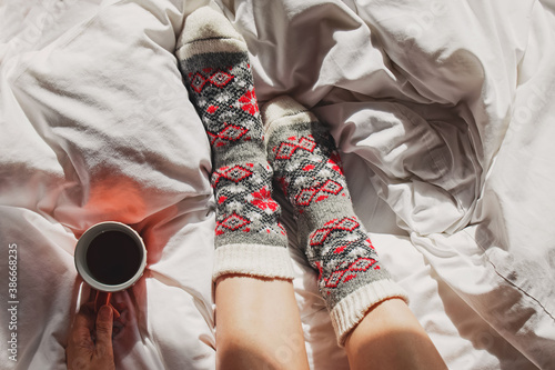 A cup of coffee or tea and female feet in warm knitted socks