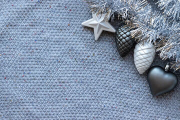 Gray knitted background with silver tinsel garland and Christmas tree toys: heart, star and pine cones